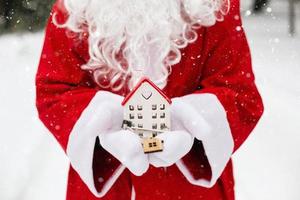 House key with keychain cottage in hands of Santa Claus outdoor in snow. Deal for real estate, purchase, construction, relocation, mortgage. Cozy home. Merry Christmas, new year booking event and hall photo