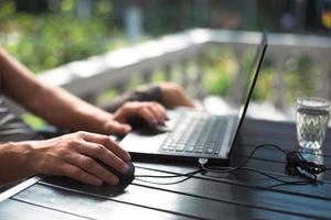 Working at a laptop in the outdoor courtyard - men's hands close-up. Home office, remote work, remote location. Using the keyboard and mouse, relax photo