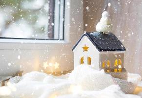 Cozy house is wrapped in a hat and scarf in a snowstorm -window sill decor. Winter, snow - home insulation, protection from cold and bad weather, room heating system. Festive mood, Christmas, New Year photo