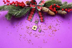 House key with keychain cottage on a festive background with Christmas tree, lights of garlands. Happy New Year-purple background, gift, greeting card. Purchase, construction, relocation, mortgage photo