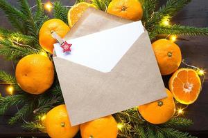 Envelope with a sheet of paper-a letter to Santa Claus, Copyspace on a Christmas background of tangerines, garlands, fir branches. Clothespin-star in place for notes. New year, wish list, dream, gifts photo