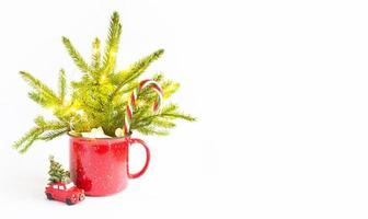 Christmas bouquet in a red mug made of live spruce and festive decorations and accessories, toys for the Christmas tree, sweets. New Year, festive mood, floristry on a white background with copy space photo