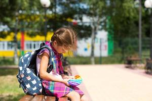 una niña pequeña con una mochila y un uniforme escolar en el patio de la escuela juega al juguete. regreso a la escuela, 1 de septiembre. el alumno se relaja después de las lecciones. educación primaria, clase elemental para estudiante foto