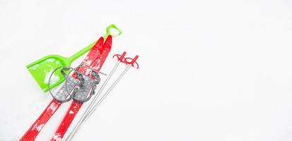 Children's red skis with sticks and a green snow shovel-layout in the snow. Winter outdoor activities, family fun. White natural frosty background. Copy space photo