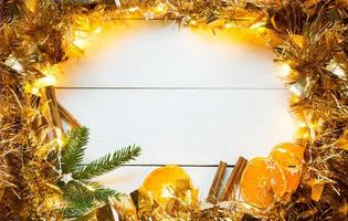 Slices of dried oranges, cinnamon sticks, fir branches. tinsel and gold garland on a white wooden background. Christmas, new year, holiday, warm autumn and winter atmosphere. Copy space, flat lay photo