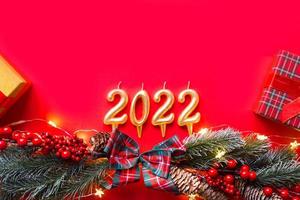 feliz año nuevo- velas doradas números 2022 en un fondo rojo con árbol de navidad, lentejuelas, estrellas, brillo, cajas de regalo. saludos, postal. calendario, portada. foto