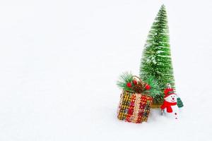A Christmas tree, a gift box and a toy snowman on white natural snow in a snowfall. Decoration for New year and Christmas, greeting card with copyspace photo