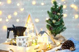 decoración navideña en la mesa con taza y cafetera. árbol de navidad, bandeja - desayuno matutino de año nuevo con luces de hadas y vasos. foto