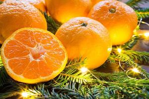 Fresh tangerines in garland lights, on fir branches and tinsel - new year's bright background. Half of an orange, citrus aroma of the holiday. Christmas, New year. Space for text. photo