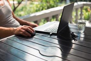 Working at a laptop in the outdoor courtyard - men's hands close-up. Home office, remote work, remote location. Using the keyboard and mouse, relax photo