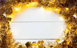 Festive frame made of gold garland with lights and tinsel on a white wooden background, copyspace. New year, Christmas, autumn and winter warming atmosphere. photo