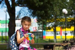 una niña pequeña con una mochila y un uniforme escolar en el patio de la escuela juega al juguete. regreso a la escuela, 1 de septiembre. el alumno se relaja después de las lecciones. educación primaria, clase elemental para estudiante foto