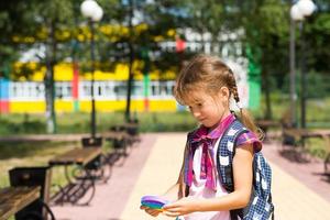 una niña pequeña con una mochila y un uniforme escolar en el patio de la escuela juega al juguete. regreso a la escuela, 1 de septiembre. el alumno se relaja después de las lecciones. educación primaria, clase elemental para estudiante foto