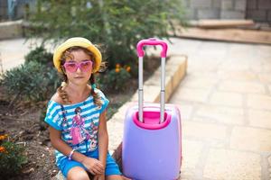 una chica con maleta, sombrero y gafas de sol se va de vacaciones. espera del viaje, llegada al lugar de residencia en el hotel. foto