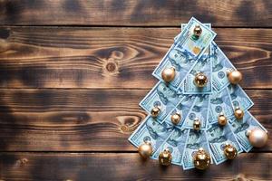 árbol de navidad hecho de billetes de 100 dólares sobre fondo de madera con copyspace. decoración navideña sobre el tema de finanzas, ahorros, riqueza, gastos en año nuevo. categóricamente. pila de 100, inversiones, negocios foto