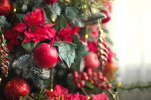 Red decor on a Christmas tree made of apples and poinsettias. Christmas background and frame for new year. Close-up, festive fir tree with berries, icicles, garlands. Space for text photo