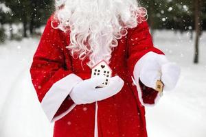 House key with keychain cottage in hands of Santa Claus outdoor in snow. Deal for real estate, purchase, construction, relocation, mortgage. Cozy home. Merry Christmas, new year booking event and hall photo