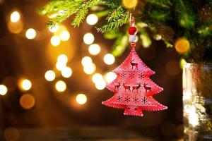 Red Christmas tree toy on a branch of a natural fir tree with lights of garlands in defocus in the background. Metal toy with slits of deer and snowflakes. Christmas, new year, copy space, bokeh. photo