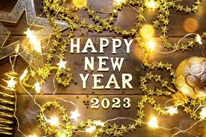 Happy New Year-wooden letters and the numbers 2023 on a festive background with sequins, stars, glitter, lights of garlands. Greetings, postcard. Calendar, cover photo