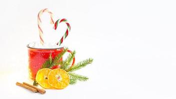 A red mug with marshmallows and candy cane in the shape of a heart is decorated with a natural fir branch or dried orange slices and cinnamon sticks. Christmas and New Year, the flavor of the holiday. photo