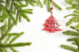 juguete rojo en forma de árbol de navidad en las ramas verdes de un abeto natural sobre un fondo blanco, marco. copie el espacio. navidad, año nuevo. decoración con ranuras en forma de ciervo, copos de nieve. foto