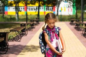 chica con mochila y una pila de libros cerca de la escuela. regreso a la escuela, el niño está cansado, pesados libros de texto. educación, clases de escuela primaria, el comienzo del año escolar, 1 de septiembre foto