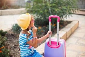 A girl with a suitcase, a hat and sunglasses is going on vacation. Waiting for the trip, arrival at the place of residence at the hotel. photo