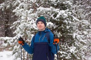 esquiador con mochila y sombrero con pompón con bastones de esquí en las manos sobre el fondo de un bosque nevado. esquí de fondo en bosque de invierno, deportes al aire libre, estilo de vida saludable, turismo de deportes de invierno. foto