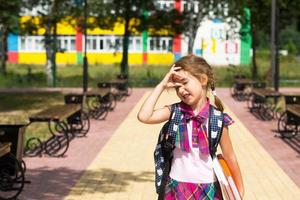 chica con mochila y una pila de libros cerca de la escuela. regreso a la escuela, el niño está cansado, pesados libros de texto. educación, clases de escuela primaria, el comienzo del año escolar, 1 de septiembre foto