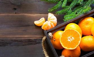 Fresh tangerines in brown box on wooden background with green fir branches. Frame, copy space, holiday and winter fragrance, new year, Christmas. Healthy food, orange juice, shop window. Slice and cut photo