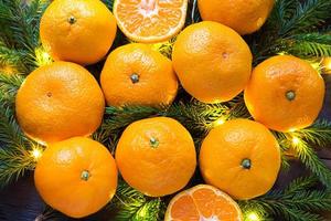 Fresh tangerines in garland lights, on fir branches and tinsel - new year's bright background. Half of an orange, citrus aroma of the holiday. Christmas, New year. Space for text. photo