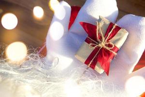 una caja con un regalo de navidad en manos de santa claus en mitones blancos. traje rojo, barba, guirnaldas de luces borrosas. año nuevo, preparación, expectativa de un milagro, un sueño hecho realidad. de cerca foto