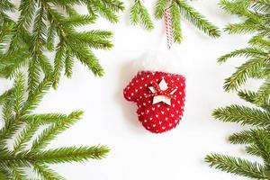 Red knitted mitten Christmas decor on a green spruce branch on a white background. Frame, copy space. Christmas new year, Christmas tree. Keep warm in winter photo