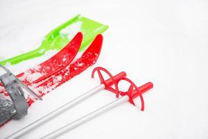 Children's red skis with sticks and a green snow shovel -layout in the snow. Winter outdoor activities, family fun. White natural frosty background. Copy space photo