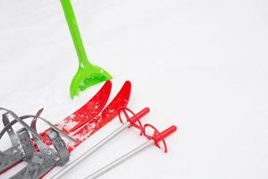 Children's red skis with sticks and a green snow shovel-layout in the snow. Winter outdoor activities, family fun. White natural frosty background. Copy space photo