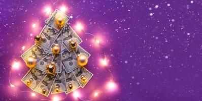 Christmas tree of 100 dollar bills on purple background with copyspace and snow, fairy lights. Decor of finance, savings, wealth, expenses in new year. Flatly. Stack of 100, Investments, business photo
