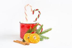 A red mug with marshmallows and candy cane in the shape of a heart is decorated with a natural fir branch or dried orange slices and cinnamon sticks. Christmas and New Year, the flavor of the holiday. photo