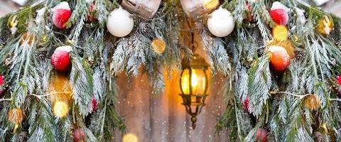 Outdoor Christmas decorations made of natural spruce branches, toys, garlands and a glowing lantern in the snow in a blizzard. Winter outside, snowfall. New Year decor