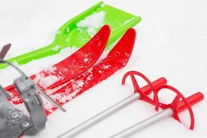 Children's red skis with sticks and a green snow shovel -layout in the snow. Winter outdoor activities, family fun. White natural frosty background. Copy space photo