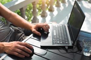 Working at a laptop in the outdoor courtyard - men's hands close-up. Home office, remote work, remote location. Using the keyboard and mouse, relax photo