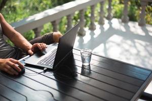 Working at a laptop in the outdoor courtyard - men's hands close-up. Home office, remote work, remote location. Using the keyboard and mouse, relax photo