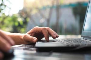 trabajando en una computadora portátil en el patio al aire libre - primer plano de las manos de los hombres. oficina en casa, trabajo remoto, ubicación remota. usando el teclado y el mouse, relájate foto