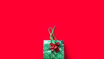 Green package with a present and a bow on a red background with copyspace. A gift for New year, Christmas, birthday, anniversary, party. Shopping photo