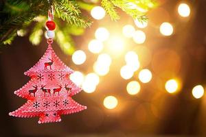 Red Christmas tree toy on a branch of a natural fir tree with lights of garlands in defocus in the background. Metal toy with slits of deer and snowflakes. Christmas, new year, copy space, bokeh. photo