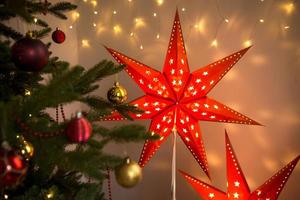 Red Christmas star-lamp on a stand. The festive decor of the interior of the house. Christmas, new year, spruce branches. Background, space for text photo