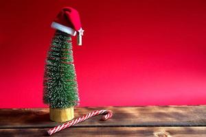 Christmas tree on a red background with lights of garlands, caramel striped cane, Santa hat, tinsel. New year, festive atmosphere. Copy space photo