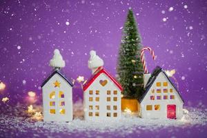 casas acogedoras y árbol de navidad en tormenta de nieve sobre fondo violeta y luces de hadas. invierno, nieve: aislamiento del hogar, protección contra el frío y el mal tiempo. estado de ánimo festivo, navidad, tarjeta de felicitación de año nuevo foto