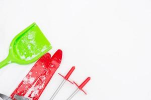 Children's red skis with sticks and a green snow shovel-layout in the snow. Winter outdoor activities, family fun. White natural frosty background. Copy space photo