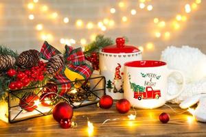 A Christmas red mug with the inscription Merry and Bright and a cookie jar on the table in a festive decor, fairy lights, branches of a Christmas tree. The mood of the new year, background photo