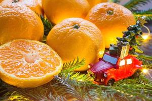 Christmas decor - red retro car carries Christmas tree with gift boxes on roof. space for text. New Year. Fresh tangerines in garland lights, on fir branches and tinsel. citrus aroma of the holiday photo